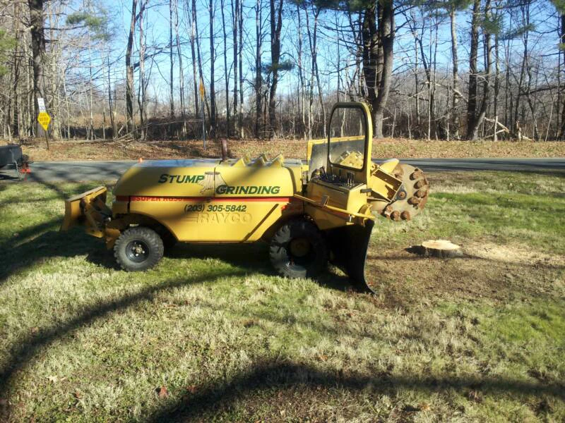 Yellow Raygo stump grinder parked on a lawn beside a ground stump
